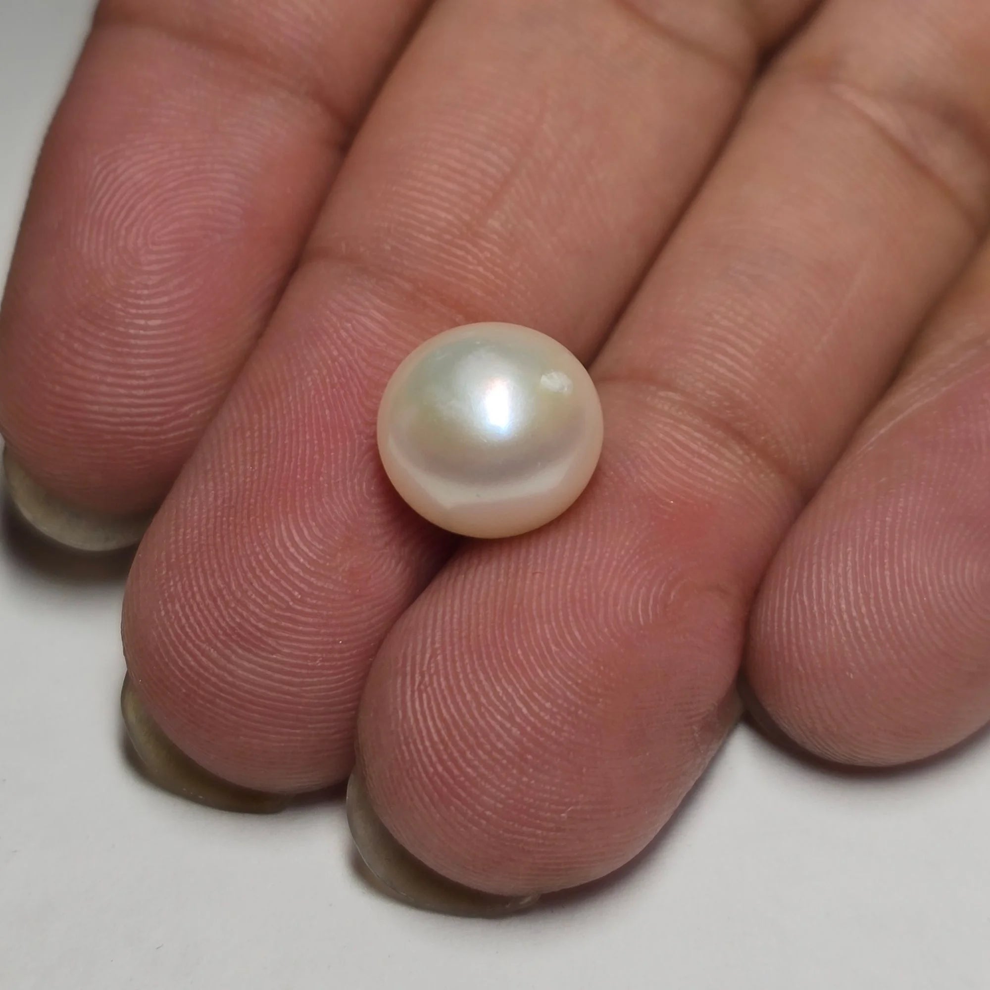 Pearl held between fingers on a white background